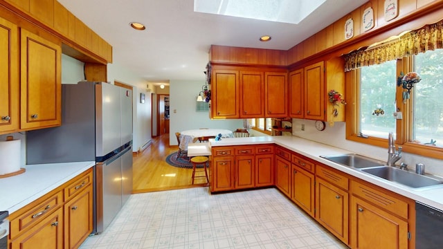 kitchen with stainless steel refrigerator, a skylight, light hardwood / wood-style flooring, sink, and black dishwasher