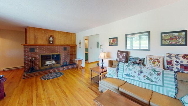 living room featuring light hardwood / wood-style flooring, baseboard heating, and a brick fireplace