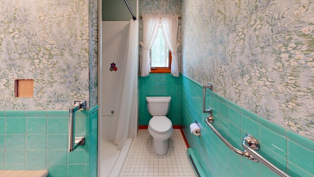 bathroom featuring toilet, walk in shower, tile patterned floors, baseboard heating, and tile walls