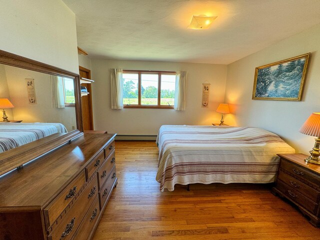 bedroom with a baseboard radiator, hardwood / wood-style flooring, and a textured ceiling