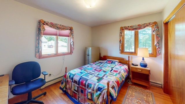 bedroom with baseboard heating, light hardwood / wood-style flooring, and a closet