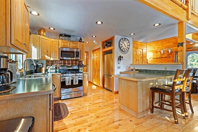 kitchen featuring sink, kitchen peninsula, a breakfast bar, appliances with stainless steel finishes, and light wood-type flooring