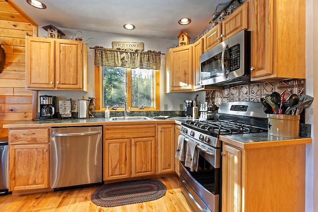 kitchen with appliances with stainless steel finishes, dark countertops, a sink, and light wood-style floors