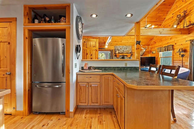 kitchen with light wood-style flooring, wooden walls, a kitchen breakfast bar, and freestanding refrigerator