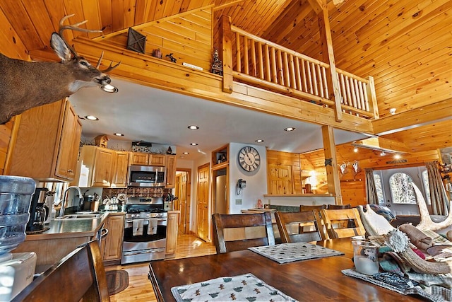 dining area with sink, wooden ceiling, a high ceiling, light hardwood / wood-style floors, and wooden walls