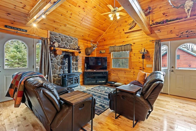 living area featuring lofted ceiling with beams, wooden ceiling, a wood stove, wood walls, and light wood-style floors