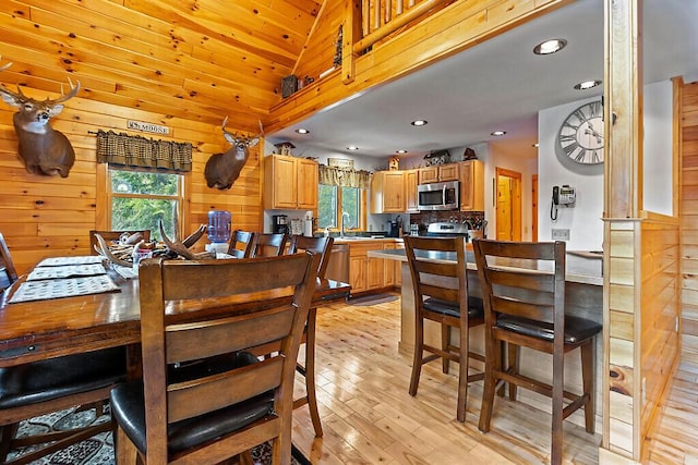 dining space featuring wood ceiling, vaulted ceiling, wooden walls, sink, and light hardwood / wood-style floors