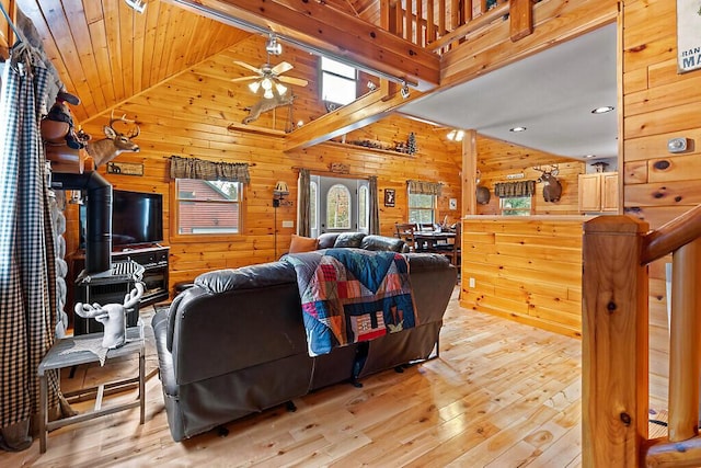 living room with ceiling fan, wooden ceiling, light hardwood / wood-style flooring, high vaulted ceiling, and wood walls