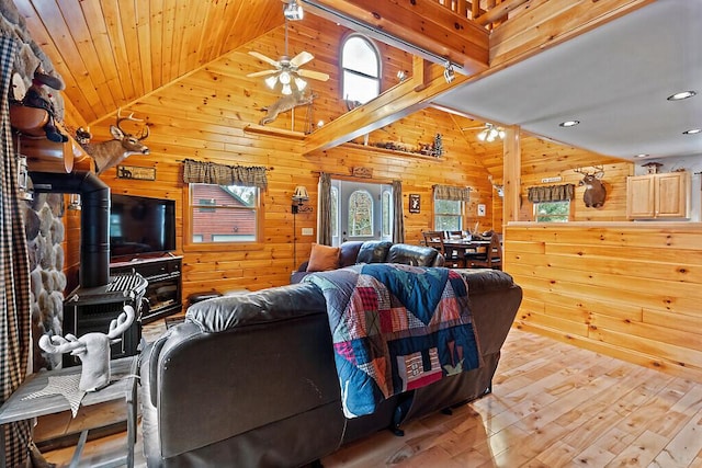 living area featuring light wood finished floors, ceiling fan, wood ceiling, a wood stove, and wood walls