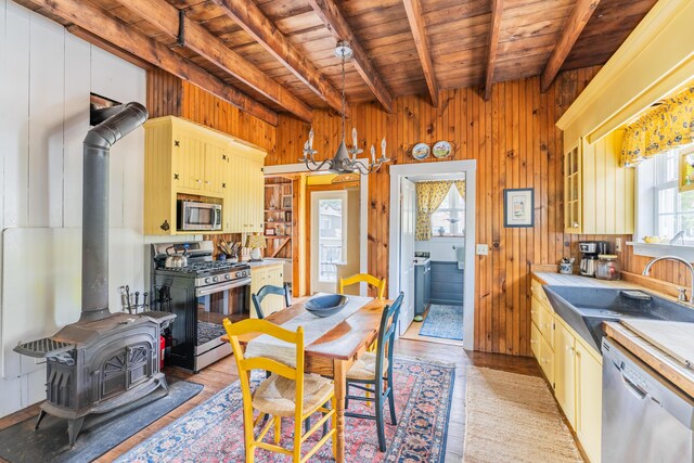 dining area with light wood-type flooring, beam ceiling, a wood stove, and wooden ceiling