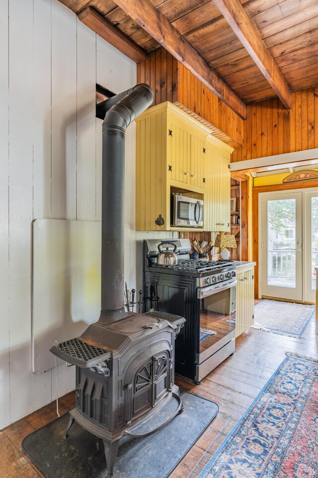 kitchen with hardwood / wood-style flooring, a wood stove, beam ceiling, appliances with stainless steel finishes, and wooden ceiling