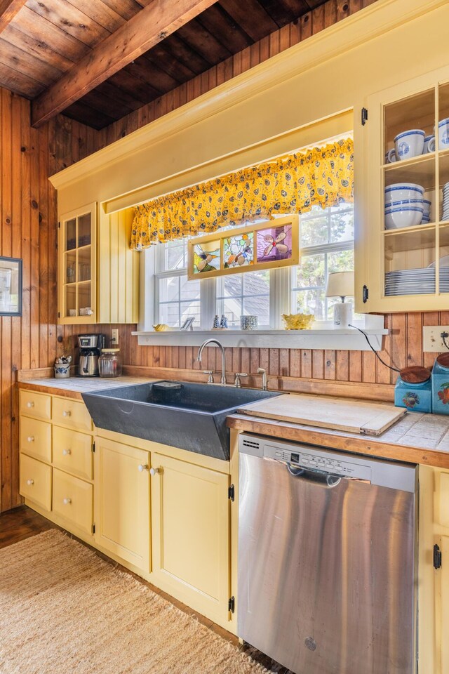 kitchen featuring beam ceiling, dishwasher, wood walls, and a healthy amount of sunlight