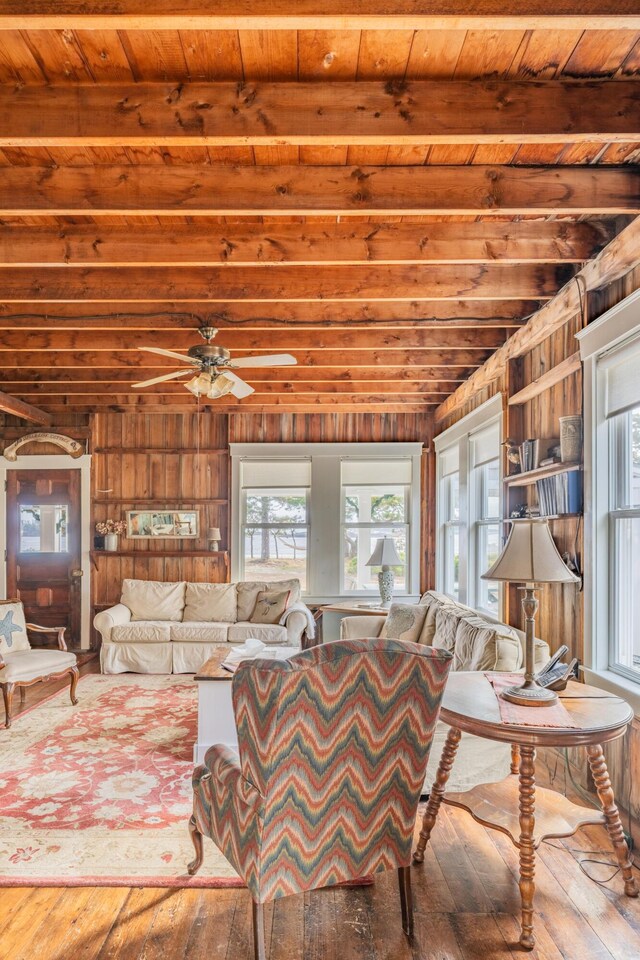 living room with beamed ceiling, wooden ceiling, wood-type flooring, ceiling fan, and wooden walls