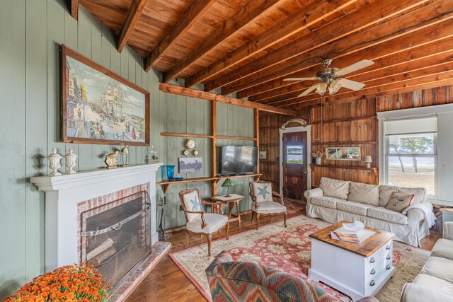 living room with a fireplace, wood walls, wood-type flooring, beam ceiling, and ceiling fan