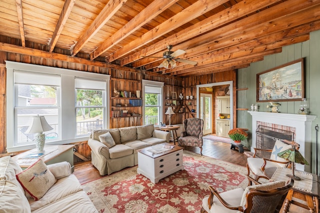 living room featuring ceiling fan, light wood-type flooring, beam ceiling, wooden walls, and a fireplace