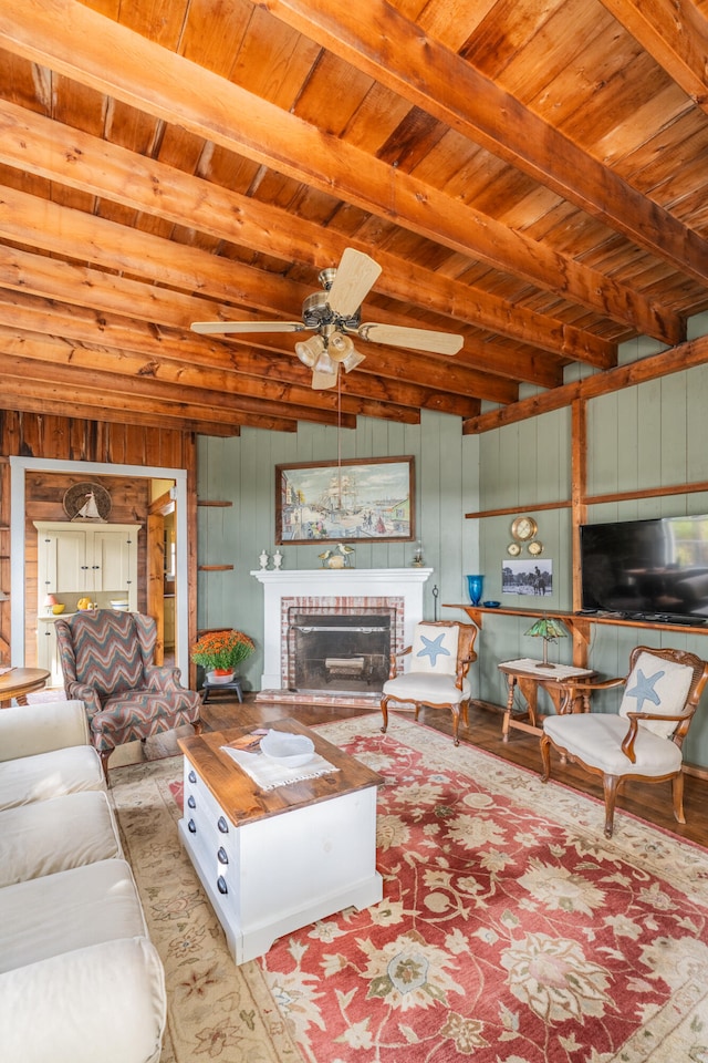 living room featuring ceiling fan, wood ceiling, wood walls, beam ceiling, and a fireplace