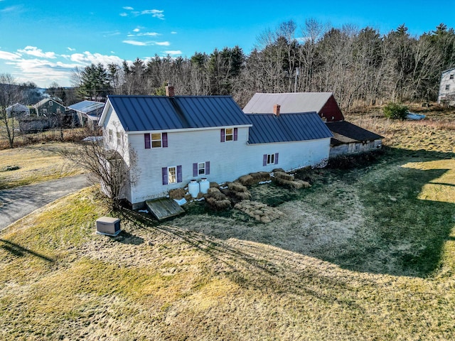 exterior space with a standing seam roof, a lawn, a chimney, and metal roof