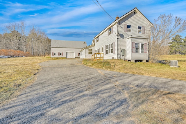 view of front of property with a front lawn, aphalt driveway, a chimney, a garage, and an outbuilding