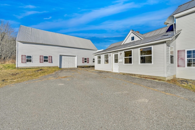 view of front of house featuring an outbuilding, a standing seam roof, an attached garage, aphalt driveway, and metal roof