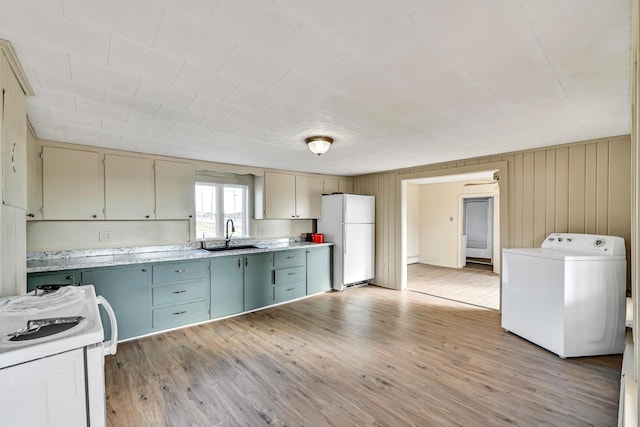 kitchen with white appliances, washer / dryer, a sink, light countertops, and light wood-type flooring