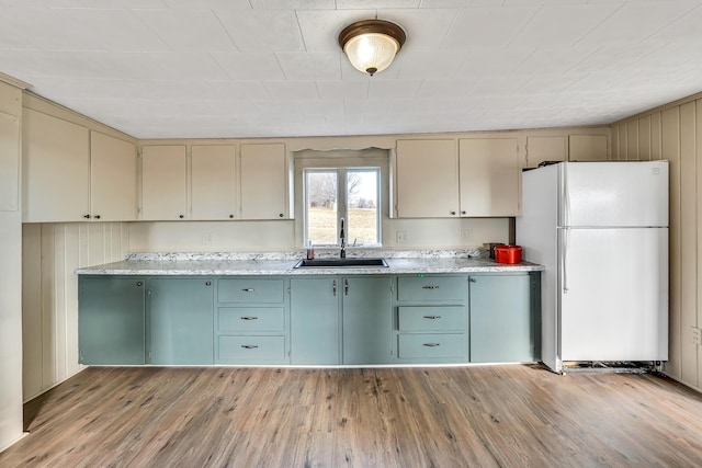 kitchen featuring cream cabinets, light wood-style floors, freestanding refrigerator, and a sink