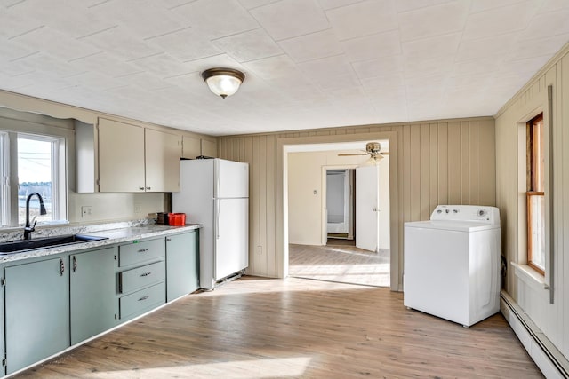 kitchen featuring a baseboard radiator, washer / dryer, freestanding refrigerator, a sink, and light wood-style floors