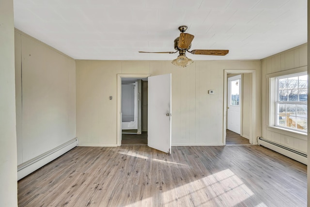 empty room with baseboard heating, wood finished floors, baseboards, and a baseboard radiator