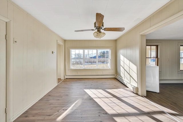 spare room with a baseboard heating unit, a ceiling fan, and wood finished floors