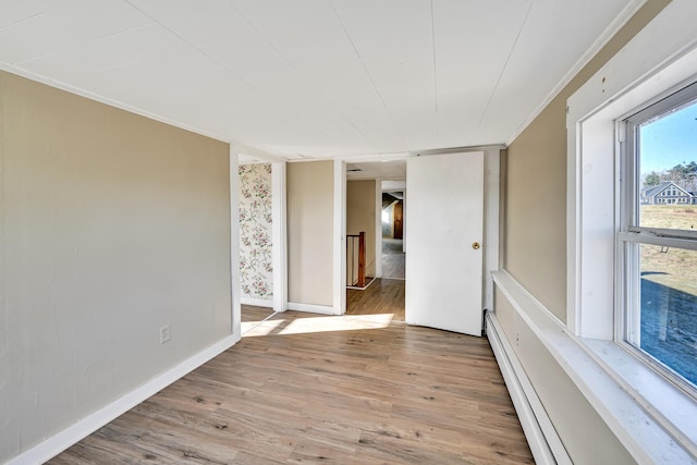 empty room featuring crown molding, light wood-style floors, baseboards, and baseboard heating