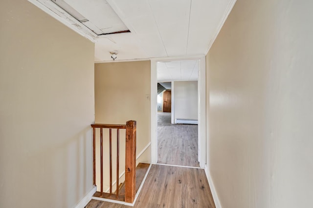 hallway featuring baseboards, wood-type flooring, crown molding, an upstairs landing, and baseboard heating