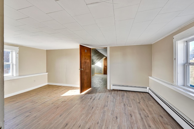 spare room featuring a baseboard heating unit, baseboards, and wood finished floors