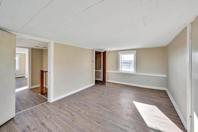 empty room with a baseboard radiator, baseboards, and wood finished floors