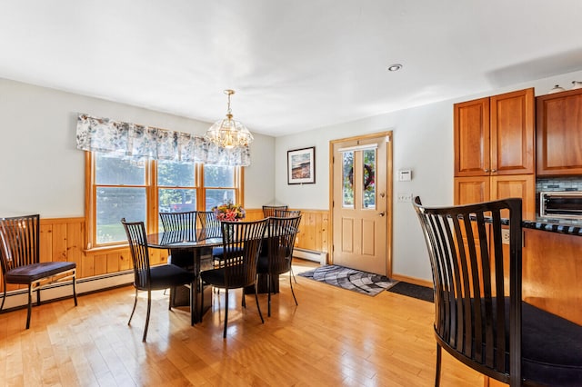 dining area with light hardwood / wood-style flooring, baseboard heating, a notable chandelier, and wooden walls