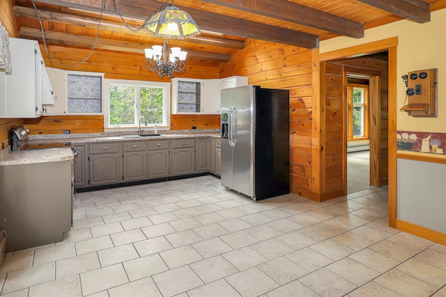 kitchen featuring stainless steel fridge, pendant lighting, wooden walls, sink, and an inviting chandelier