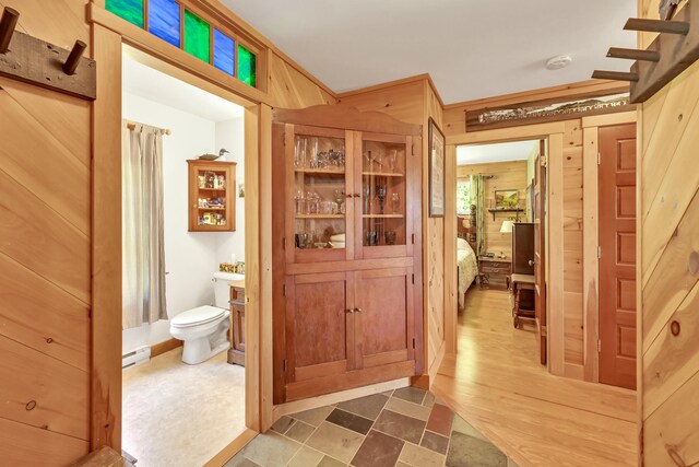 bathroom featuring a baseboard radiator, toilet, wood-type flooring, and wooden walls