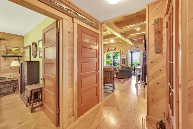 hall with wood ceiling, beamed ceiling, wooden walls, and light hardwood / wood-style floors