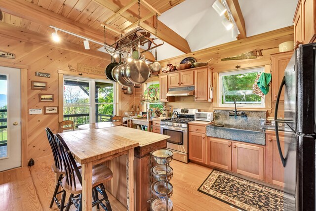 kitchen with black fridge, plenty of natural light, stainless steel range with gas stovetop, and wooden walls