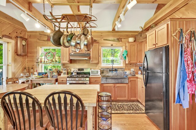 kitchen featuring light brown cabinetry, wooden walls, light hardwood / wood-style floors, black refrigerator, and stainless steel range with gas cooktop