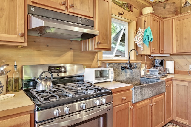 kitchen with a toaster, light countertops, under cabinet range hood, stainless steel gas range oven, and tasteful backsplash