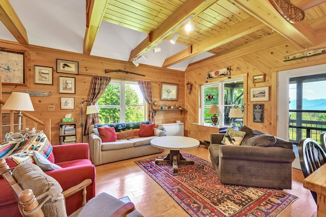 living room with wooden walls, lofted ceiling with beams, track lighting, and light hardwood / wood-style floors