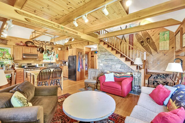 living room featuring rail lighting, hardwood / wood-style flooring, wooden walls, and beamed ceiling