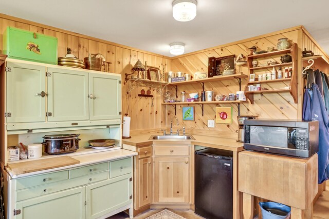 kitchen with green cabinets, black dishwasher, wooden walls, and sink