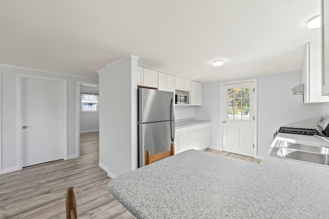 kitchen featuring sink, white cabinets, stove, light hardwood / wood-style flooring, and stainless steel fridge