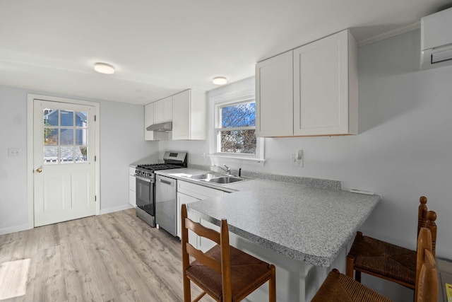 kitchen featuring a breakfast bar, white cabinets, stainless steel gas range oven, light hardwood / wood-style flooring, and sink