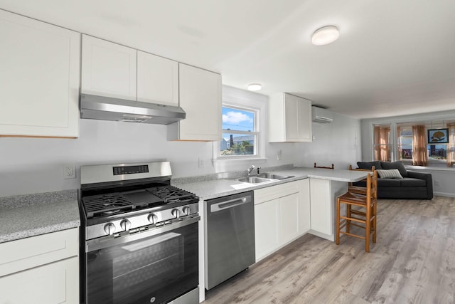 kitchen with a wall unit AC, sink, white cabinetry, light hardwood / wood-style flooring, and appliances with stainless steel finishes