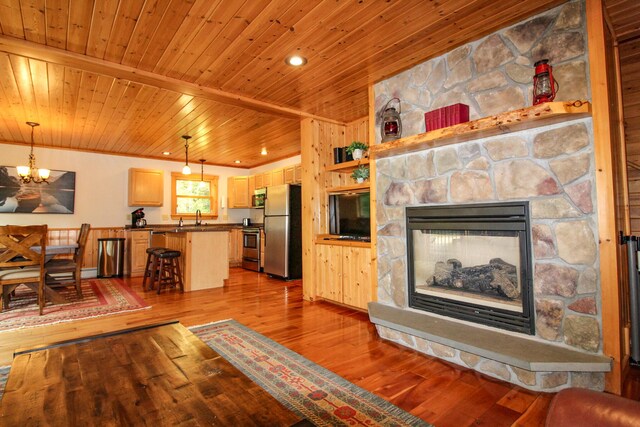 living room with hardwood / wood-style floors, a chandelier, sink, a stone fireplace, and wood ceiling