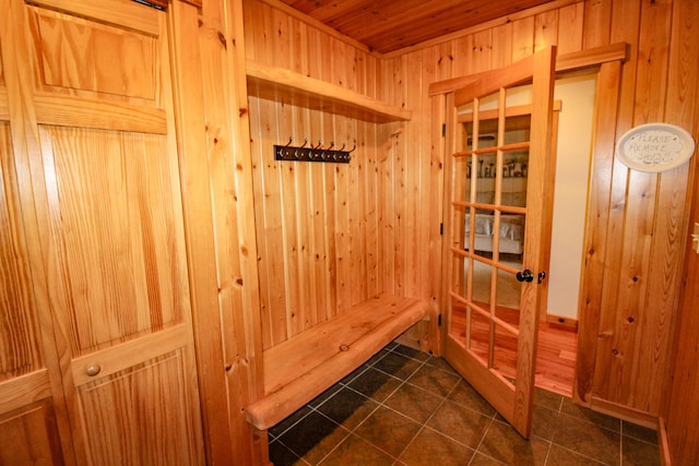 mudroom with dark tile patterned floors and wooden walls