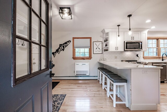 kitchen featuring kitchen peninsula, white cabinets, stainless steel appliances, and decorative light fixtures