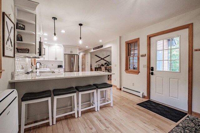 kitchen with white cabinets, pendant lighting, kitchen peninsula, stainless steel refrigerator, and a baseboard radiator