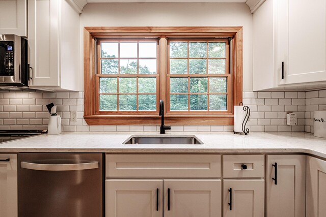 kitchen with sink, backsplash, white cabinetry, appliances with stainless steel finishes, and light stone countertops